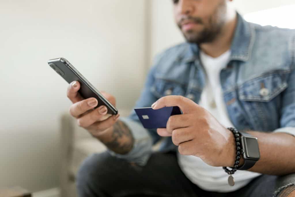 Man holding credit card and phone, sitting on a couch at home