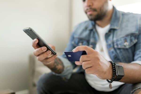 Man holding credit card and phone, sitting on a couch at home